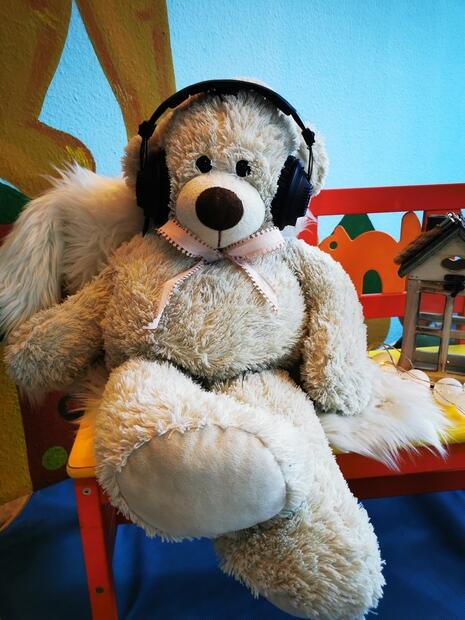 Ein Teddybär mit Kopfhörern sitzt auf einer roten Holzbank.